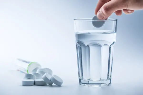 Magnesium pills and cup of clear water on blue white background.