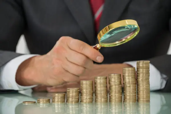 Businessman Holding Magnifier On Coin At Desk Inflação é maior dor de cabeça para 43% dos leitores