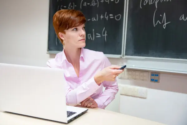 Portrait of young female teacher at school lesson with blackboard in background