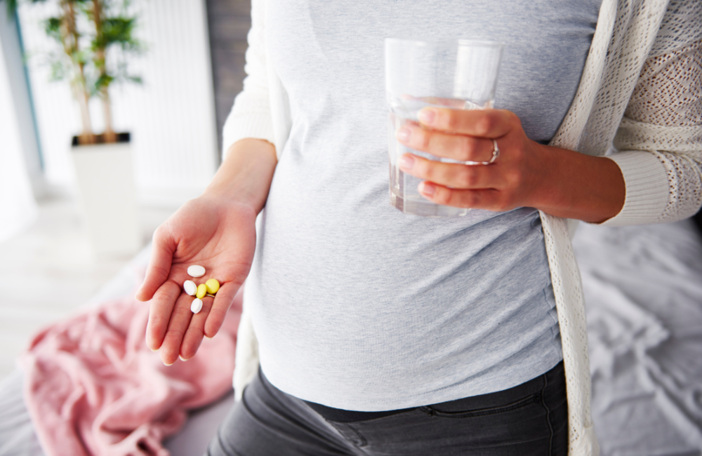 Mulher grávida com remédios e um copo de água na mão mostrando que grávida pode tomar dramin